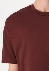 Bordeaux katoenen t-shirt met een klassieke ronde halslijn en omgeslagen korte mouwen, gladde textuur met een schoon, eenvoudig ontwerp.