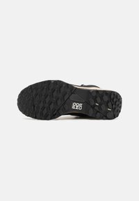 Black rubber shoe sole with multi-directional hexagonal tread pattern, featuring brand logo. Smooth edge with reinforced heel area.