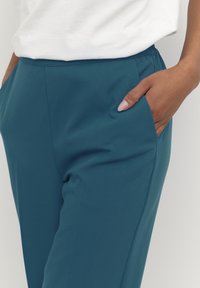 Teal broeken met een gladde textuur, voorzien van een fitted ontwerp en zijzakken. De tailleband zit op de natuurlijke taille en complementiseert casual kleding.