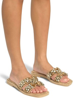 Sandali scivolati beige con suola piatta, caratterizzati da un gruppo decorativo di strass trasparenti e dorati sulle cinghie incrociate.