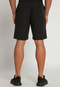 Un short noir avec une taille élastique, des ourlets retroussés et deux poches arrière. Le modèle porte également des chaussures de sport noires.