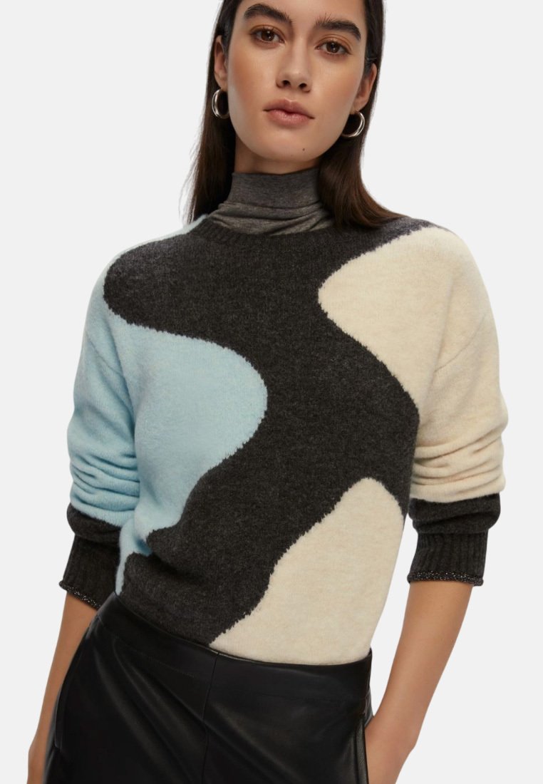 Maglione lavorato a maglia con onde nere, azzurre e crema. Collo alto, polsini a costine e texture morbida. Abbinato a una gonna di pelle.