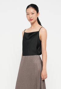 Svart satin camisole med tynne stropper, kombinert med et lyst grått plisserte skjørt med subtile detaljer. Glatte teksturer og elegant design.