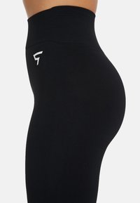 Korkeavyötäröiset mustat leggingsit, jotka on valmistettu joustavasta kankaasta ja joissa on sileä pinta. Sivussa valkoinen logo. Muotoon käyvä malli.