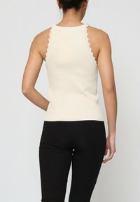 Débardeur en crème avec des bretelles festonnées, design ajusté et ourlet droit. Associé à des leggings noirs à côtes.