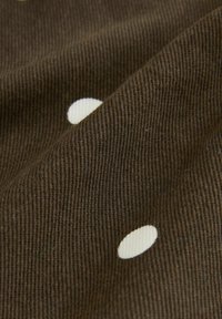 Bruine corduroy stof met witte polka dots, met zichtbare textuur en plooidetails.