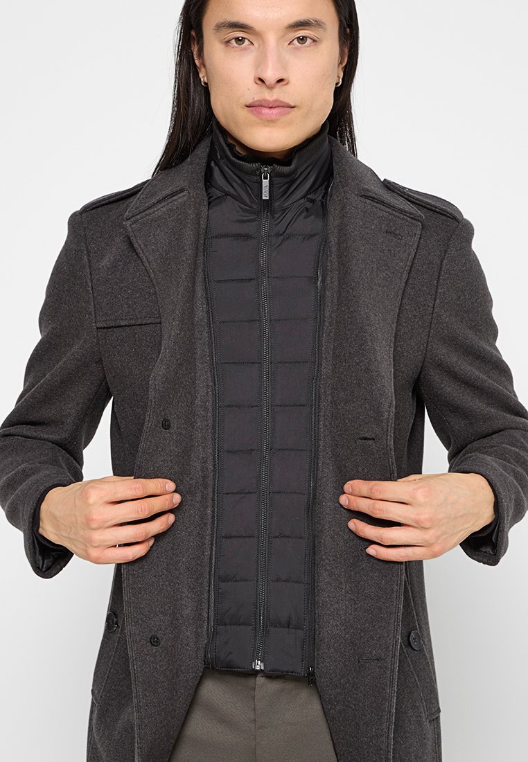 Abrigo de lana gris con una chaqueta acolchada negra ajustada debajo. Presenta un diseño de doble botonadura, solapas con muesca y bolsillos laterales.