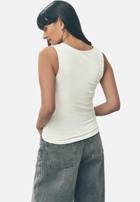 Haut blanc sans manches avec un col rond, assorti à un pantalon en denim gris taille haute. La texture semble lisse et ajustée.