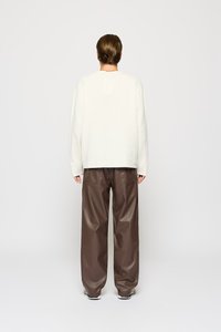 Sudadera crema de gran tamaño y pantalones de cuero marrón holgados. Los detalles notables incluyen un escote amplio y un diseño minimalista.