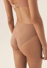 Nude seamless high-waisted brief made of smooth fabric, featuring a minimalistic design and subtle stitching along the edges.