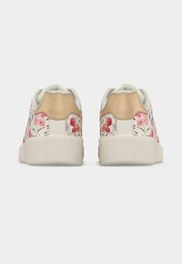 Ζευγάρια λευκών αθλητικών παπουτσιών με ροζ και κόκκινα λουλουδάτα σχέδια και μπεζ υφασμένες ταμπάδες στο τακούνι, εμφανιζόμενα από πίσω σε λευκό φόντο.