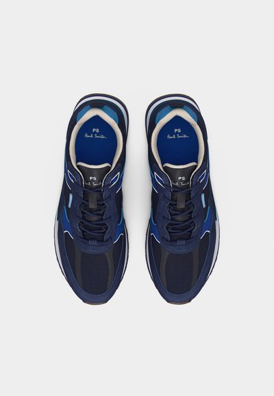 Ζευγάρι ναυτικών μπλε αθλητικών παπουτσιών Paul Smith με μαύρες και μπλε λεπτομέρειες, λευκή επένδυση και εσωτερικές σόλες με σήμανση, φαινόμενα από πάνω σε λευκό φόντο.
