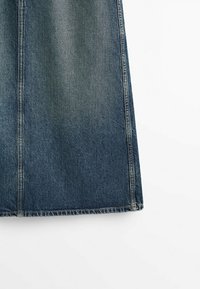 Section d'une jupe en denim bleu foncé montrant des coutures verticales et une texture délavée sur fond blanc.