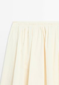 Krämfärgad plisserad kjol med vertikala ränder. Elastisk midja upptill, mjuk textur och flödande design skapar volym.