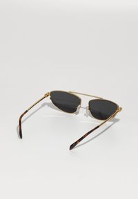 Ochelari de soare cu lentile întunecate, ramă din metal auriu și brațe cu model țestoasă. Prezintă pernuțe pentru nas și un design subțire cu dublu pod.