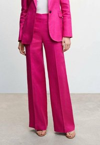 Różowe lniane spodnie o szerokich nogawkach i wysokim stanie, o gładkiej teksturze i prostych liniach. W komplecie z pasującą marynarką i sandałami.