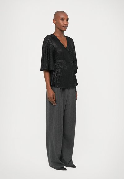 Blouse noire texturée avec un décolleté en V et des manches larges, associée à un pantalon gris ample taille haute, rehaussé par une ceinture.