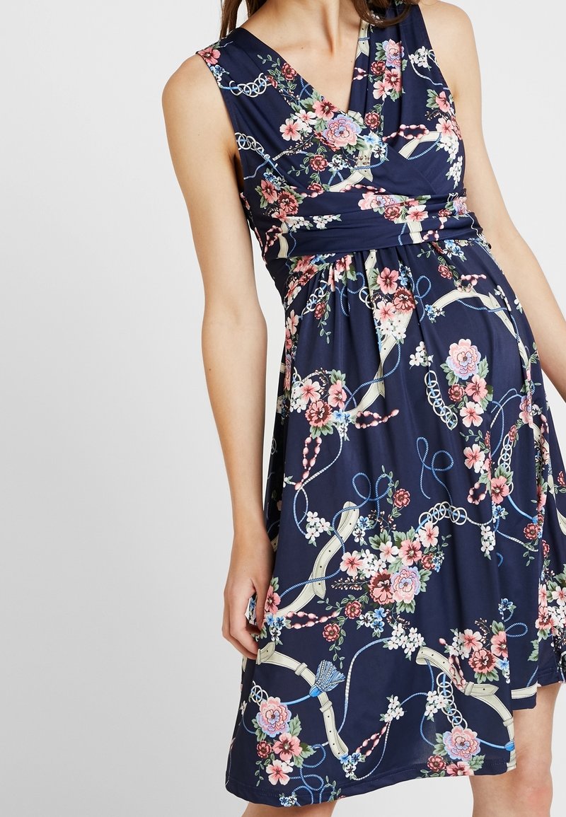 Robe bleu marine sans manches avec col en V et taille froncée, présentant un motif floral et ruban dans des tons rose, blanc et bleu.
