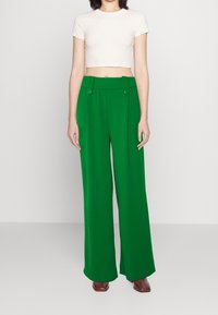 Pantalon vert à jambes larges et taille haute, doté de boutons à la taille et d'une texture lisse, accompagné d'un top court crème ajusté.