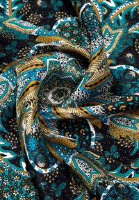 Tejido colorido que presenta intrincados patrones de paisley en turquesa, dorado y blanco sobre un fondo negro, con una textura suave y pliegues caídos.