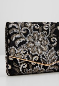 Černá sametová kabelka s vyšíváním květin ve zlaté a stříbrné barvě, s flitry a zlatou ozdobnou lištou přes přední část.