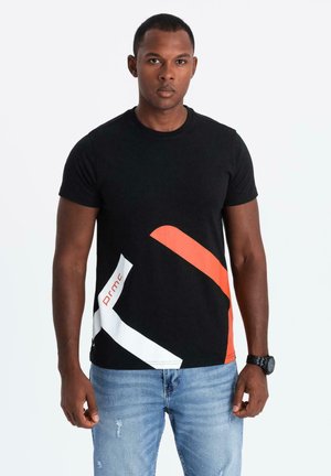 Camiseta negra de algodón con elementos de diseño gráfico curvados en rojo y blanco. Mangas cortas y escote redondo, combinada con jeans claros desgastados.