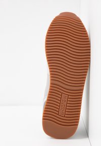 Semelle de chaussure avec une semelle en caoutchouc marron présentant des rainures ondulées et le logo "U.S. Polo Assn" embossé au centre.