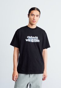 Sort bomulds t-shirt med korte ærmer, der har et hvidt grafisk print af "Carhartt WIP 1989" på fronten. Afslappet pasform.