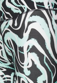 Leggings negros con un patrón de remolino fluido en verde menta y blanco, hechos de una tela suave y elástica con detalles de costura en contraste.