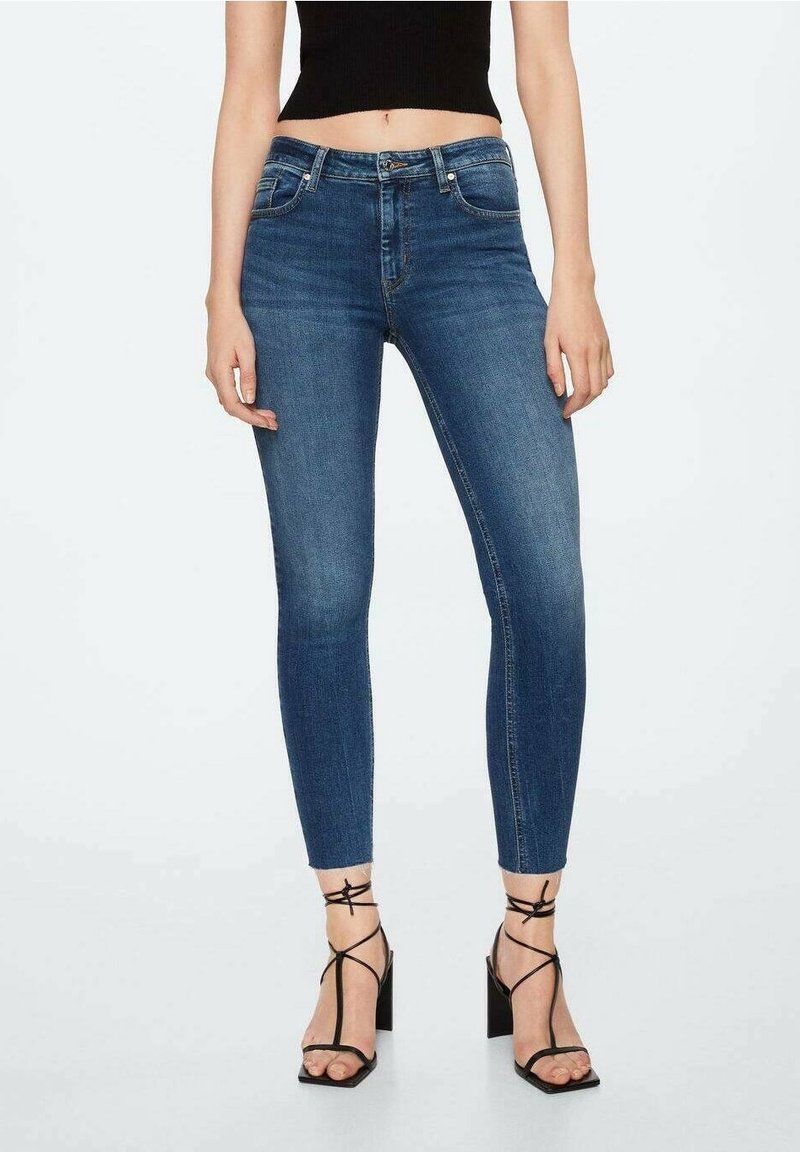 Jeans skinny en denim bleu foncé avec une taille mi-haute, dotés de poches avant et d'un design classique à cinq poches, associés à des talons noirs à lanières.