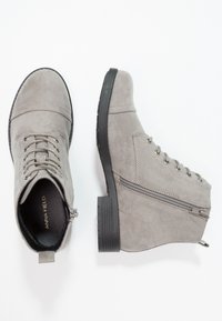 Stivaletti in suede grigio con punta rotonda, lacci, cerniera laterale e suola in gomma nera. Presentano dettagli di cucitura e una fodera in tessuto.