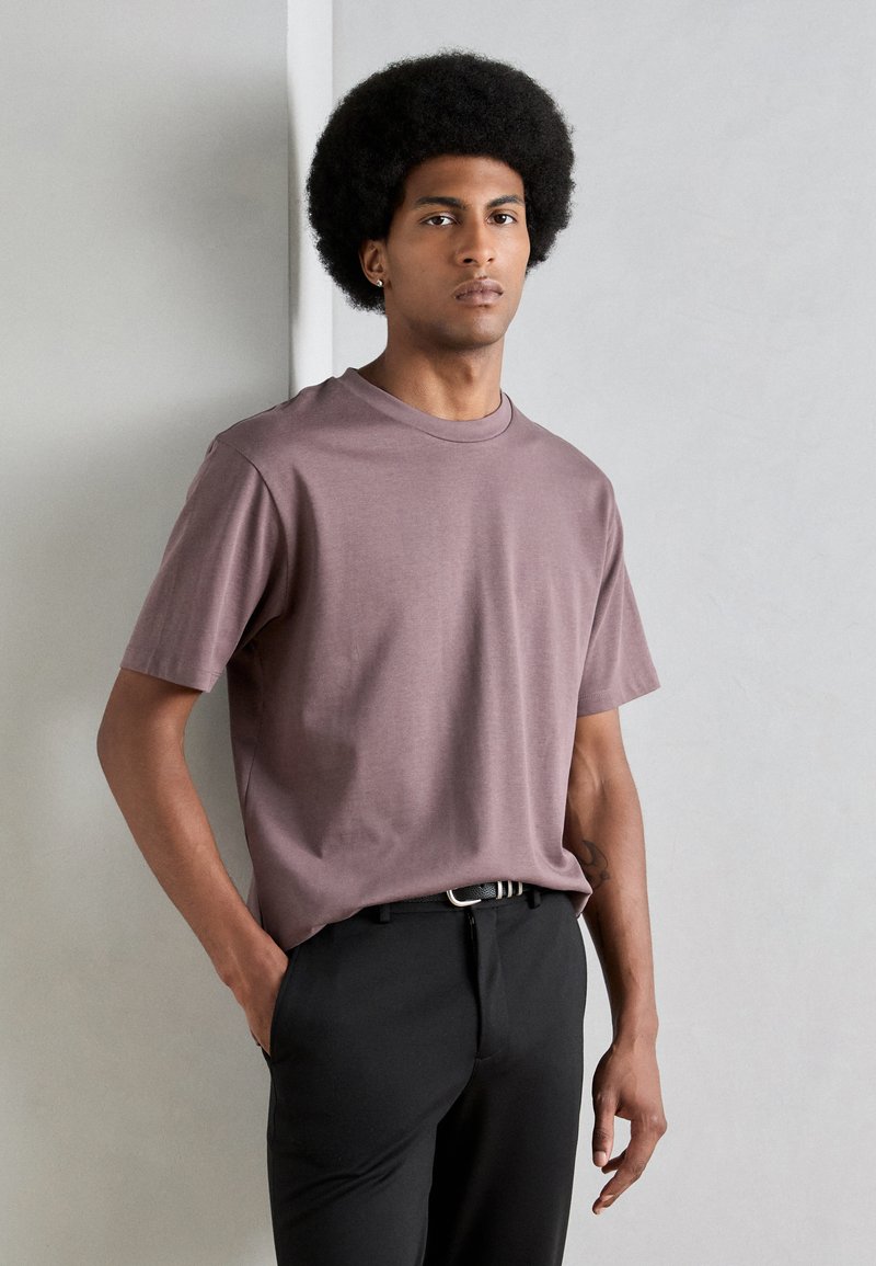 Tricou cu mânecă scurtă, de tip crew-neck, dintr-un material mauve estompat, asortat cu pantaloni negri; prezintă o textură netedă și o croială lejeră.