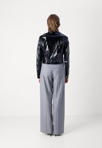 Fekete lakkbőr cropped dzseki sima felülettel, amely magas derekú, szürke, bő nadrággal van párosítva. Minimalista dizájn, látható hardver nélkül.