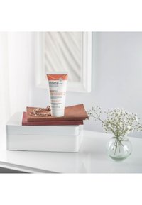 Tubo de crema hidratante Clineral SKINPRO sobre materiales apilados en tonos marrón y blanco, con una pulsera de plata y un pequeño jarrón de cristal con flores.