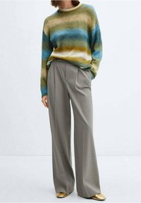 Maglione a righe in tonalità di blu, verde e giallo, abbinato a pantaloni grigi a gamba larga. Texture morbida, vestibilità rilassata e scarpe con accenti dorati.