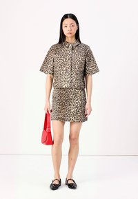 Camisa de padrão de leopardo e saia combinando em tons de castanho e preto, acompanhadas de uma mala vermelha. A modelo usa sapatilhas pretas. Design simples de mangas curtas.