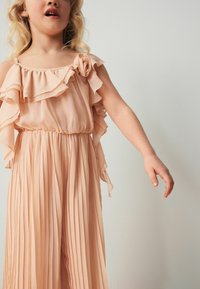 Robe plissée couleur pêche avec des accents de volants aux épaules et une taille élastique. Tissu léger, design fluide et texture douce.