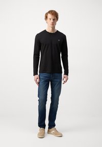 Sort langærmet T-shirt med rund halsudskæring, parret med blå denimjeans og lyse brune sneakers. Minimalistisk design, ingen mønstre.
