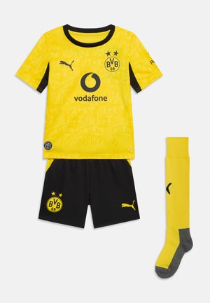 Keltamusta Borussia Dortmundin jalkapallovarustus, jossa Vodafone- ja Puma-logot, sisältäen pelipaidan, shortsit ja keltaiset sukat harmailla pohjilla.