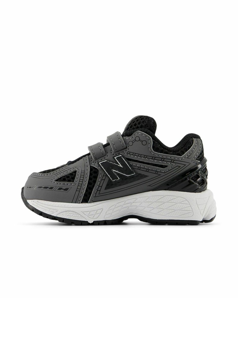 Chaussure de sport noire et grise avec tige en mesh, superpositions synthétiques, bande velcro et semelle en caoutchouc texturé blanche. Présente un logo "N" stylisé.