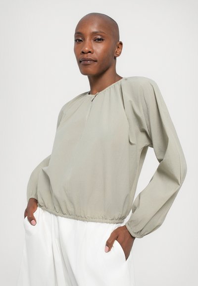 Maglietta grigia chiaro a maniche lunghe con scollo arricciato e orlo elastico, caratterizzata da una vestibilità comoda e un tessuto testurizzato. Abbinate a pantaloni bianchi larghi.