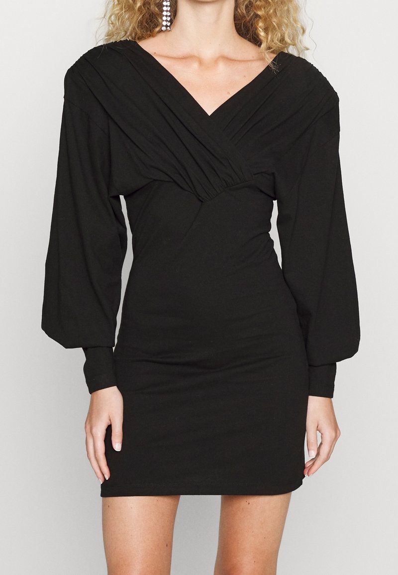 Robe moulante noire avec manches longues bouffantes et décolleté profond en V. Présente un détail de tissu froncé au niveau de la poitrine et une silhouette ajustée.