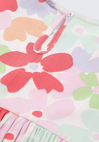 Tissu à motifs floraux dans des couleurs pastel douces, avec des fleurs rouges, roses, vertes et lavande. Comprend un détail de volant froncé au bas.