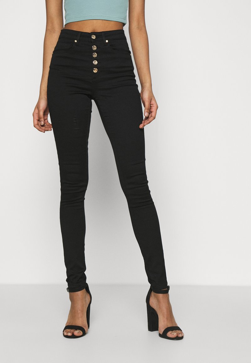 Hoch geschnittene schwarze Skinny-Jeans mit Knopfverschluss, zwei Vordertaschen und tailliertem Schnitt. Der Stoff hat eine glatte Textur.