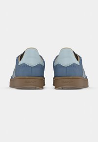 Paire de baskets décontractées bleues avec languettes de talon bleu clair et semelles marron texturées, vues de dos sur un fond uni.