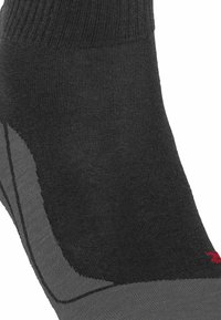 Schwarze und graue Socke mit geripptem Bündchen, nahtloser Zehenkonstruktion und verstärktem Fersenbereich. Mit einem roten Markierungsdetail an der Seite.