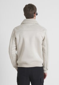 Svijetlosmeđa kožna jakna s krznom oko ovratnika, rebrastim manžetama i rubom. Glatka tekstura, ravni kroj i minimalistički dizajn.