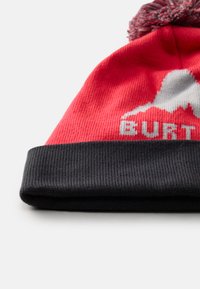 Rode gebreide beanie met zwarte omslag en pompon. Voorzien van een bergafbeelding en "BURTON" tekst in het grijs. Ribbelstructuur overal.