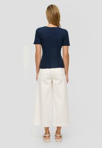 Marineblauw geribbelde top met korte mouwen gecombineerd met wijde crèmekleurige broek. De top heeft geschulpte randen; de broek heeft achterzakken en rafelige zoom.