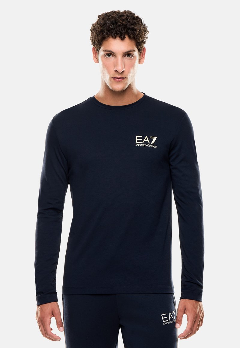 Maglietta a maniche lunghe blu navy realizzata in tessuto morbido, con un piccolo logo dorato EA7 sul petto e un collo rotondo.